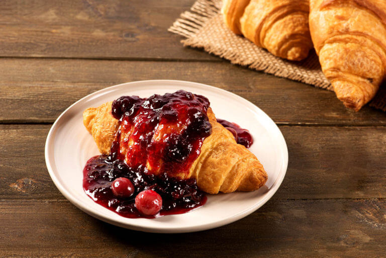 Breakfast croissant with cherry jam on a rustic background