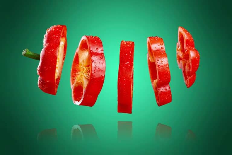 Sliced red bell pepper with reflection, isolated on a green and
